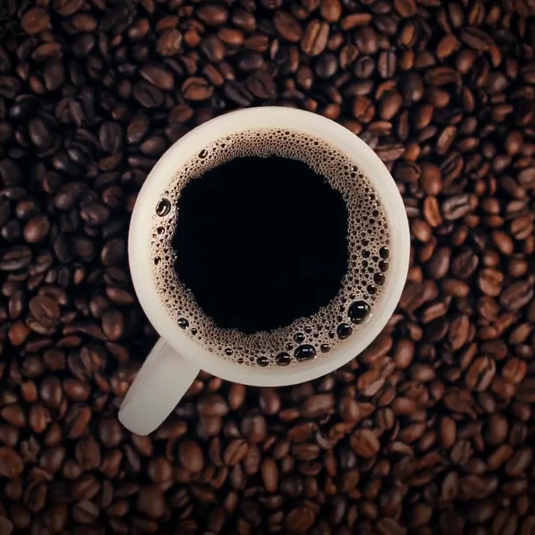 A cup of black coffee seen from above, resting on roasted beans